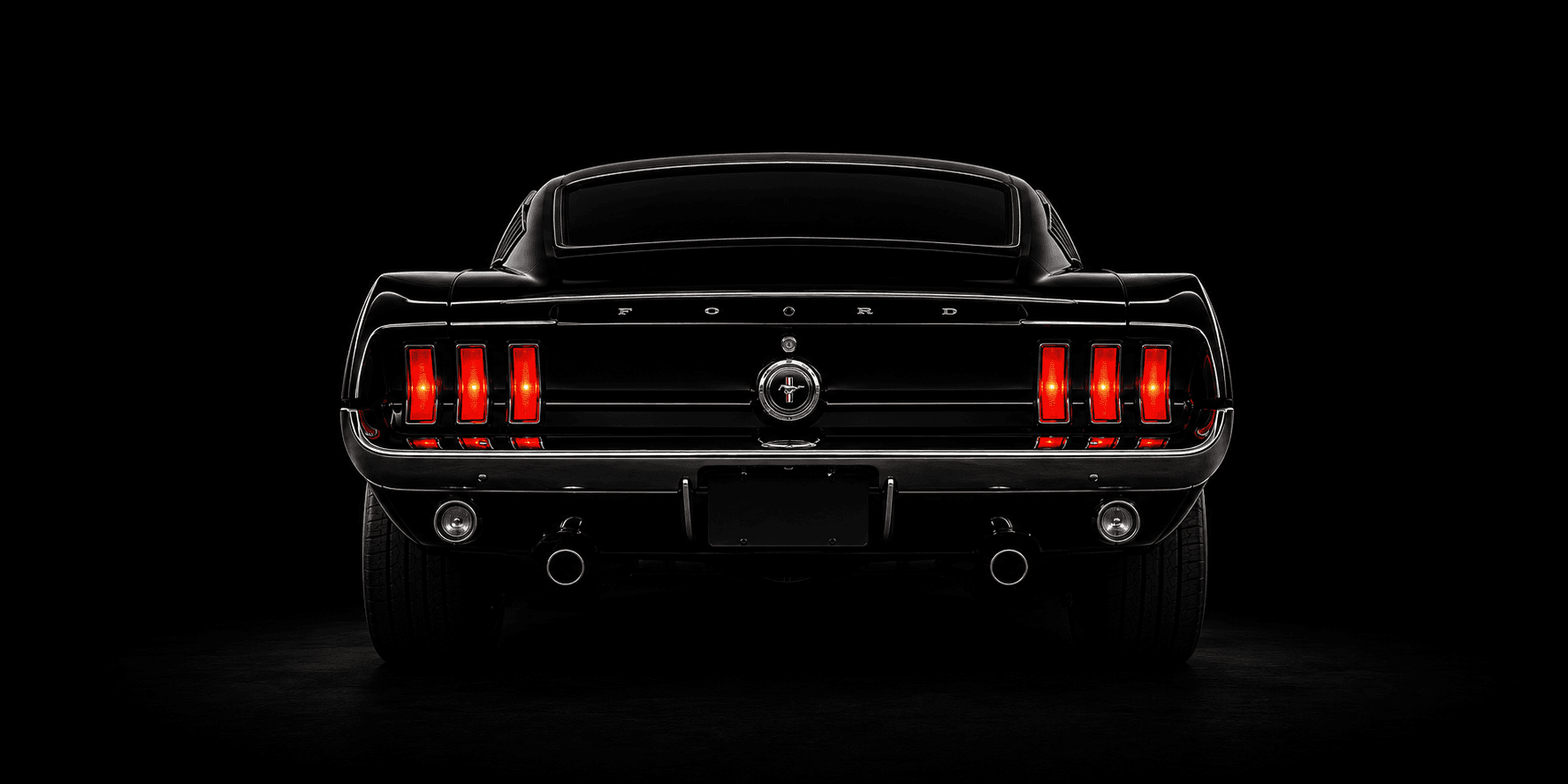 Vista trasera de un Ford Mustang negro clásico con luces rojas iluminadas sobre fondo oscuro.